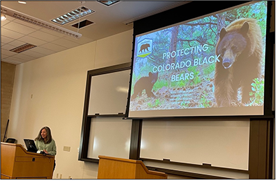 speaker at podium in front of image of bears on screen
