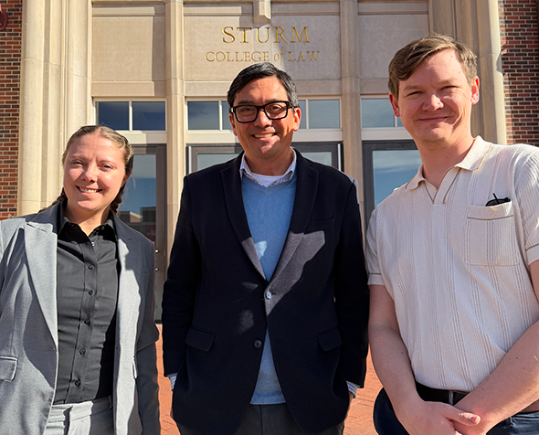 Three individuals standing in front of Sturm College of Law building