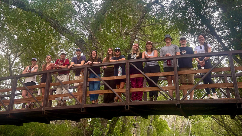 Members of Environmental Law Clinic leaning against rails of bridge with trees in background