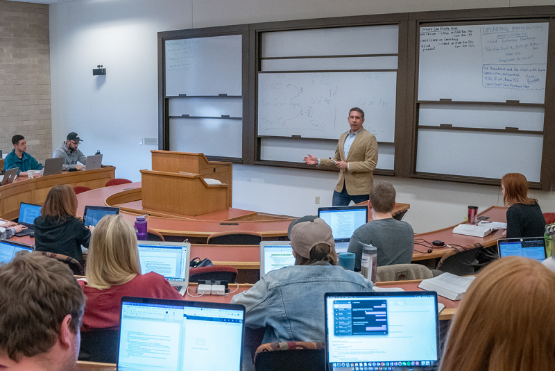 Professor in front of white board at front of classroom with students