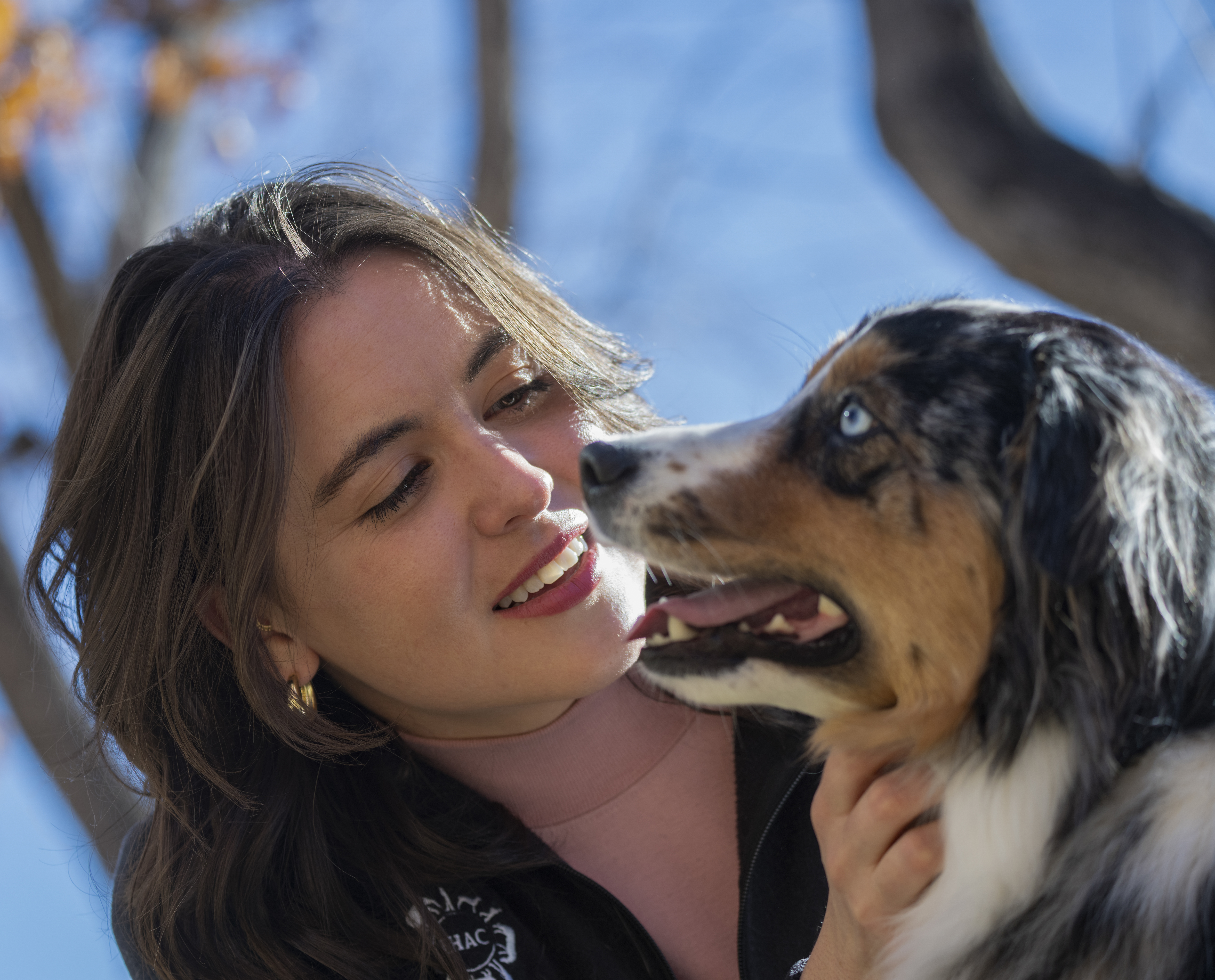 Close-up photo of a woman and a dog's face together as they interact.